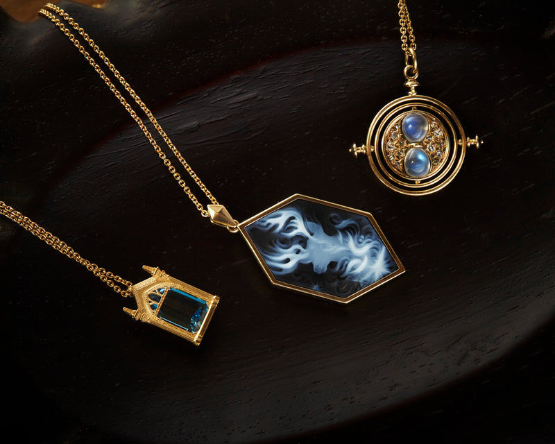  Officially licensed Harry Potter fine jewelry resting on a black background, featuring Mirror of Erised necklace, Harry's Stag Patronus cameo necklace, Time turner spinning necklace in solid 14k gold 