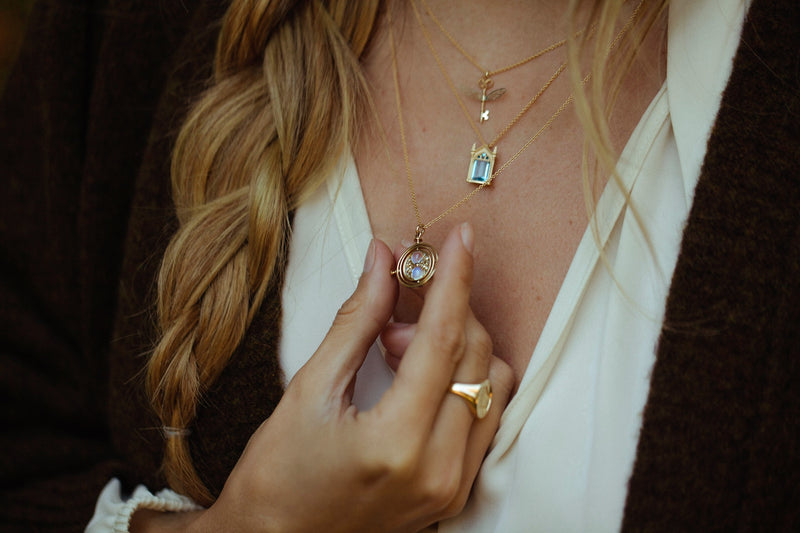 Model wearing 4 pieces of officially licensed Harry Potter fine jewelry, to include: Winged Key, Mirror of Erised, and Time Turner pendants, as well as a Hogwarts Crest Signet ring, all in 14k yellow gold. Also available in other precious metals. 