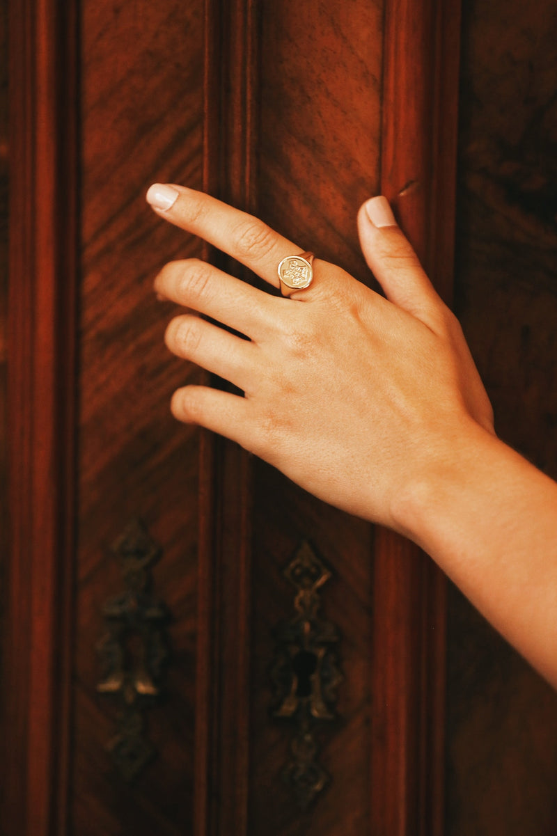 Officially licensed Harry Potter Hogwarts Crest Ring in solid 14k yellow gold on a model's hand over an oak door. 