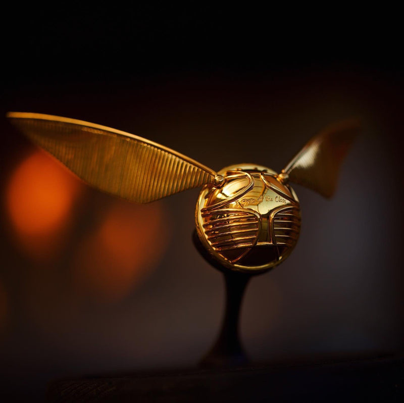 Officially licensed Harry Potter Golden Snitch Ring box in 14k yellow gold resting on its stand over a blurred background. Also available in gold plated sterling silver and platinum. 
