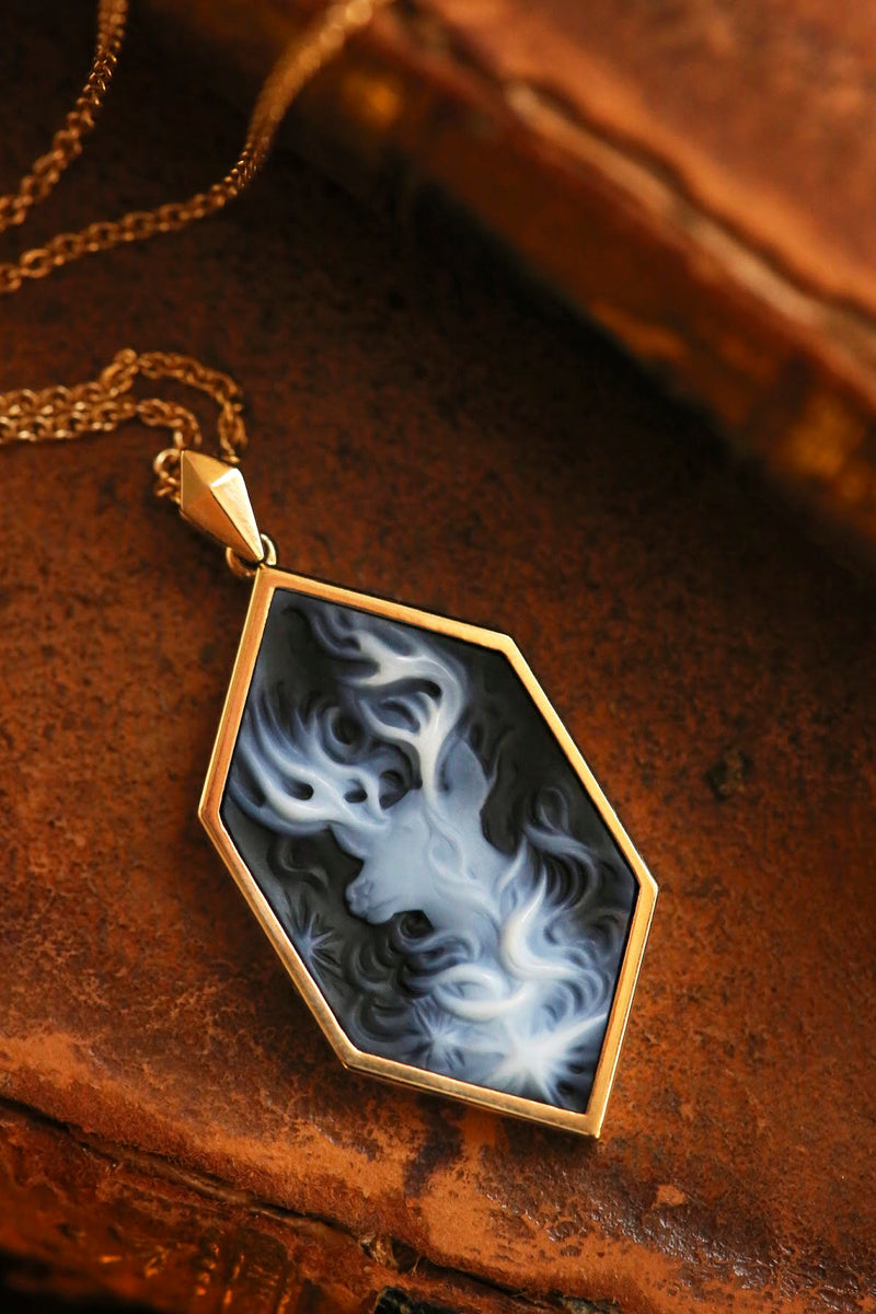 Officially licensed Harry Potter Patronus Cameo Necklace featuring a hand carved agate set in solid 14k gold resting on the back of an old leather-bound book. Also available in sterling silver, 14k white gold, 18k yellow gold, and platinum.